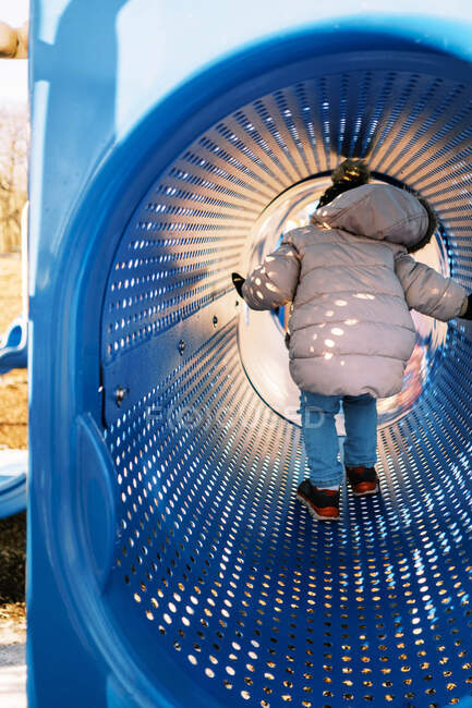 Little toddler girl climbing through tunnel at playground in winter — Stock Photo