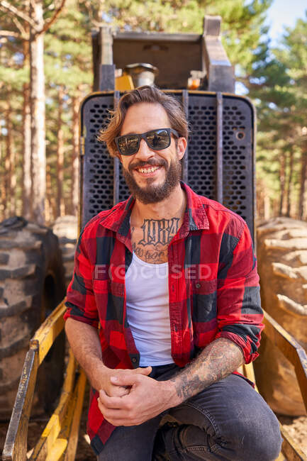 Portrait of young tattoed man leaning on against an excavator — Stock Photo