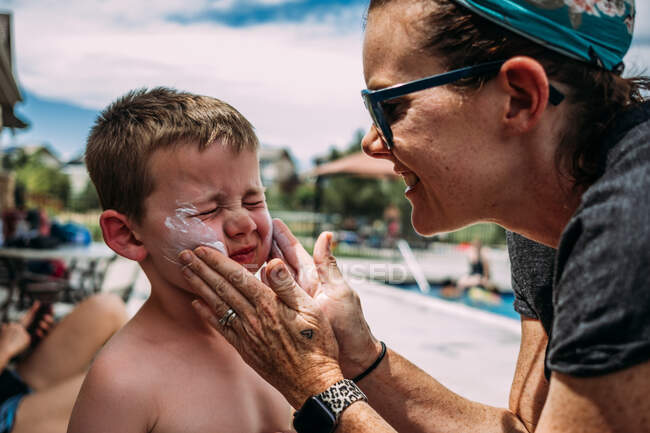 Close up de mãe colocando protetor solar nas bochechas do menino na piscina — Fotografia de Stock
