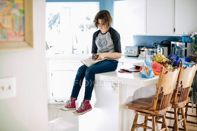 Teen girl sits on kitchen counter and places her bookmark in her book — Stock Photo