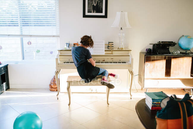 Adolescente chica se sienta en un banco de piano inapropiadamente mientras toca el piano - foto de stock