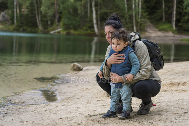 Mother with baby boy looking away at lakeshore while hiking in f — Stock Photo
