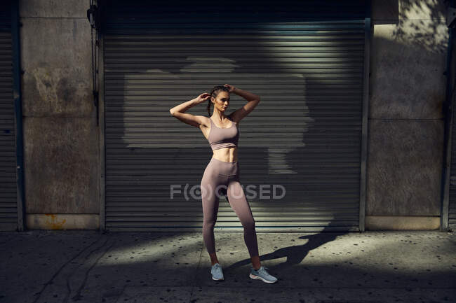 Retrato de hermosa mujer joven en ropa deportiva moderna con estilo posando en la calle de la ciudad - foto de stock
