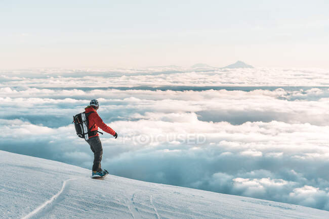 Snowboarder riding down mountain at sunset above clouds — Stock Photo