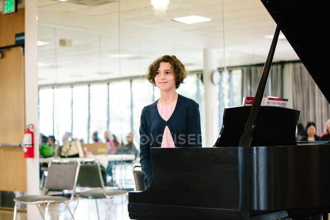 Adolescente sorri e fica ao lado de um piano de cauda após seu recital — Fotografia de Stock