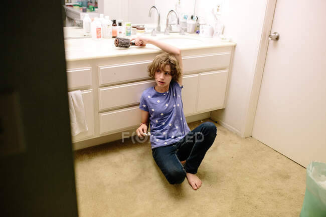 Adolescente chica sostiene cepillo de dientes y alcanza para un cepillo de pelo mientras está sentado - foto de stock