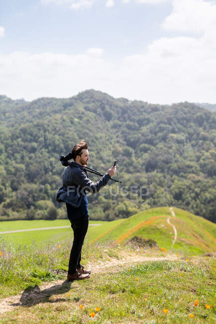Young man takes photo with phone while holding camera over shoulder — Stock Photo