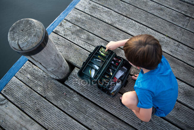Мальчик смотрит через рыболовный снаряд на деревянном причале. — стоковое фото