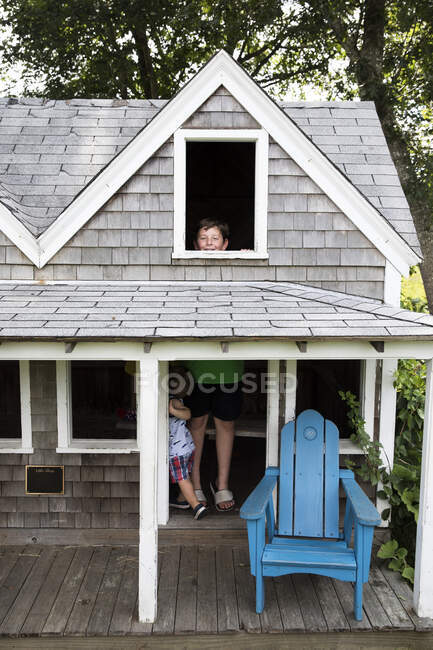 Lachender Teenie-Junge steht in humorvoll kleinem Haus und schaut aus Fenster — Stockfoto