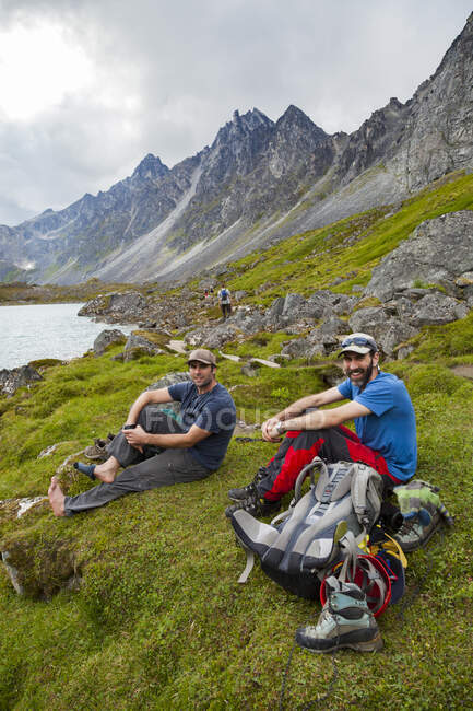 Los excursionistas se relajan en la orilla del lago Upper Reed, montañas Talkeetna, Alaska - foto de stock
