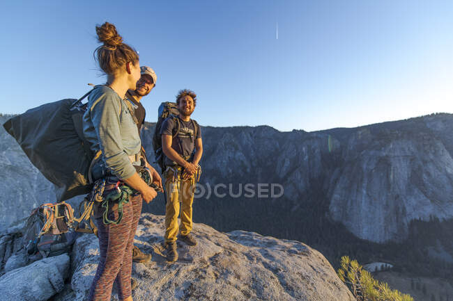 Tres excursionistas en la cima de El Capitán en el Valle de Yosemite al atardecer - foto de stock