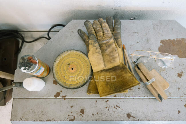 Guanti sporchi riposano da occhiali e strumenti e risorse artigianali assortiti — Foto stock