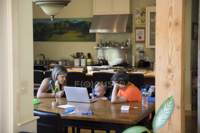 Ampla vista da mãe na mesa com filho da criança no laptop e adolescente primo — Fotografia de Stock
