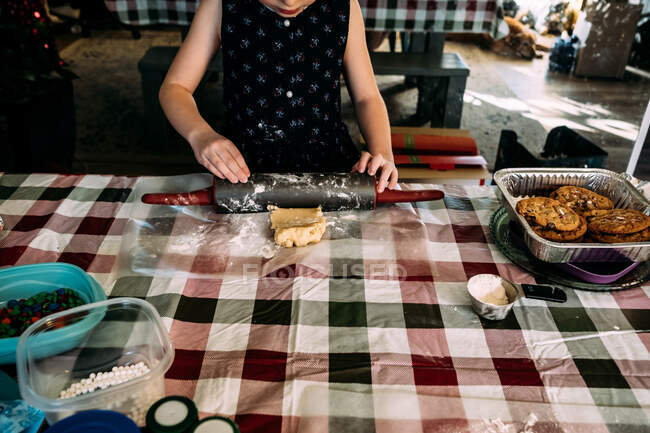 Chica joven rodando masa de galletas en la mesa del comedor - foto de stock