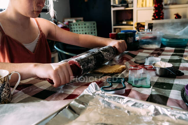 Chica adolescente rodando masa de galletas en la mesa del comedor - foto de stock