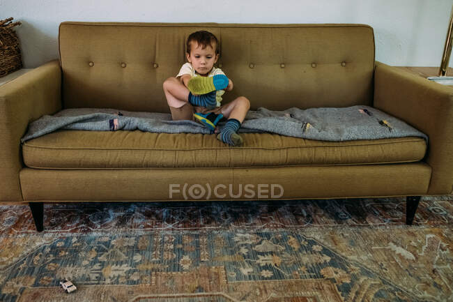 Мальчик сидит на диване и обувается. — стоковое фото