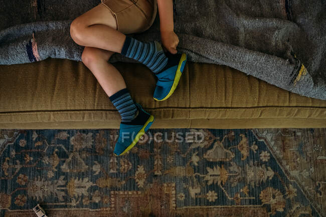 Niño sentado en el sofá poniéndose zapatos - foto de stock