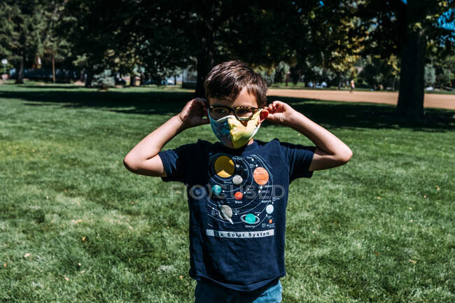 Крупним планом молодий хлопчик регулює маску для обличчя в парку — стокове фото