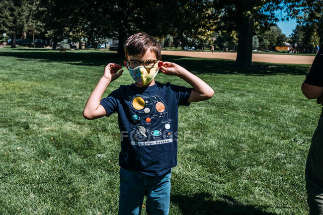 Молодий хлопчик налаштував маску для обличчя надворі в парку в сонячний день — стокове фото