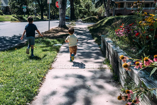 Two young boys running on a sidewalk in neighborhood — Stock Photo