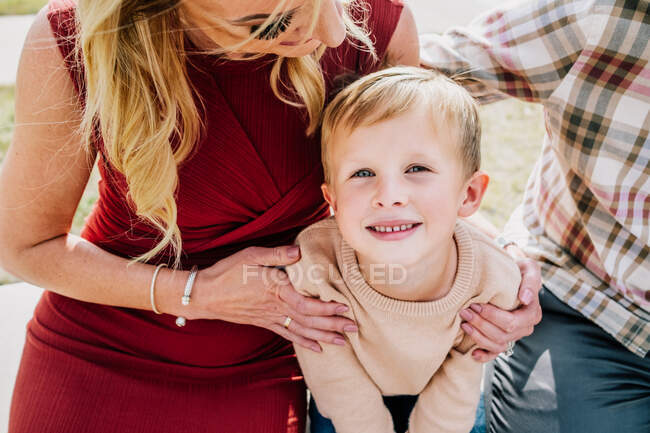 Feliz jovencito acurrucándose con sus padres afuera - foto de stock
