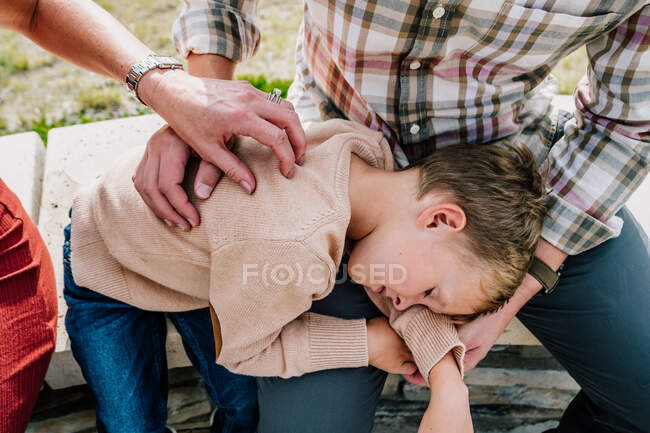 Padres reconfortando a su hijo pequeño afuera en un día soleado - foto de stock