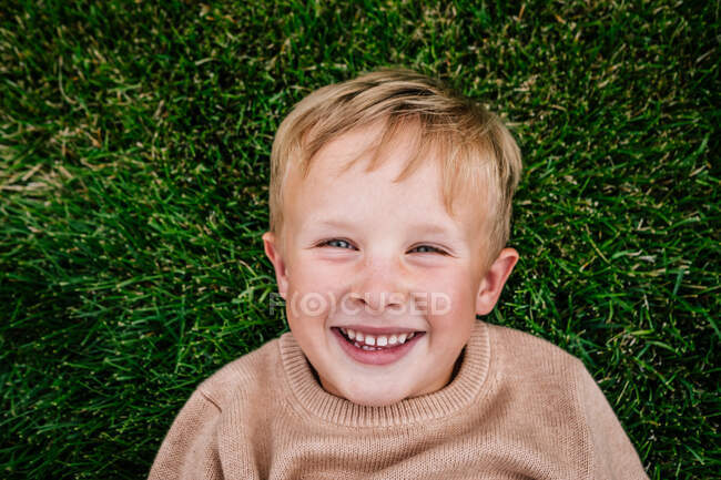 Felice giovane ragazzo posa in erba sorridente — Foto stock