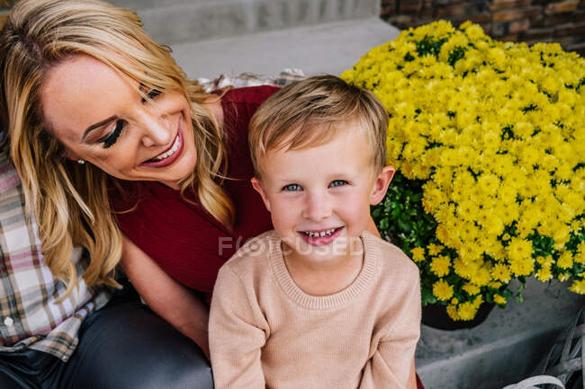 Счастливый мальчик, сидящий на маминых коленях улыбаясь — стоковое фото