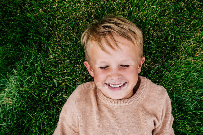Улыбающийся мальчик, лежащий в траве снаружи — стоковое фото