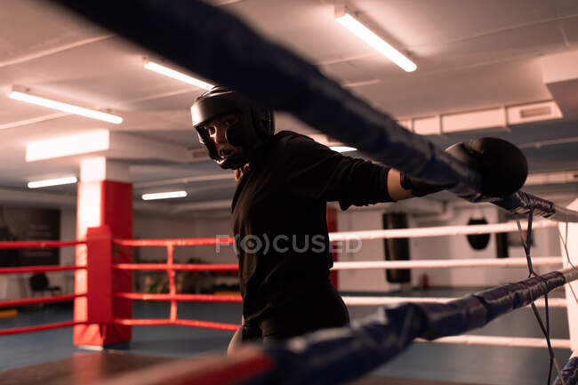 Donna forte in tenuta protettiva e abbigliamento sportivo in piedi sul ring di pugilato prima della partita in palestra moderna — Foto stock