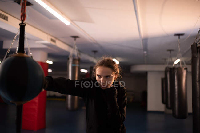 Strong female athlete performing powerful jab punch on heavy bag during boxing training in gym — Stock Photo