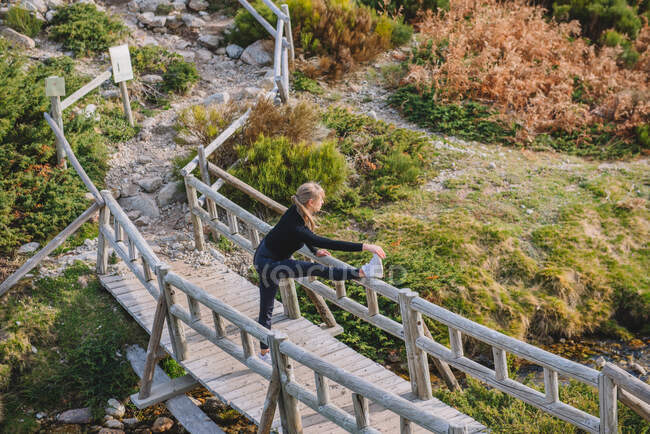 Спортсменка робить, що тягнеться на дерев'яному мосту в горах — стокове фото