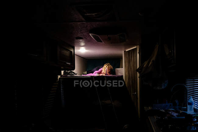 Little girl reading at night on top bunk in travel trailer camping — Stock Photo