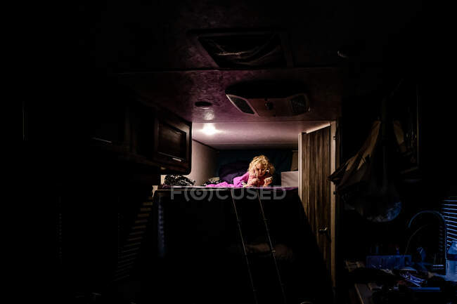 Little girl laying on top bunk reading during a camping trip — Stock Photo