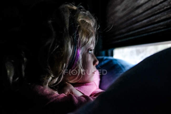 Kleines Mädchen, das vor dem Fenster auf dem Bett liegend frühmorgens ruhig schaut — Stockfoto