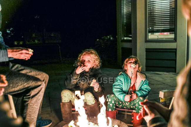 Meninas sentadas em torno do fogo pit comer marshmallows assados — Fotografia de Stock