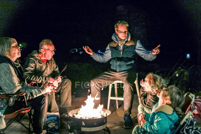 Família reunindo em torno do fogo fora contando histórias e comendo — Fotografia de Stock