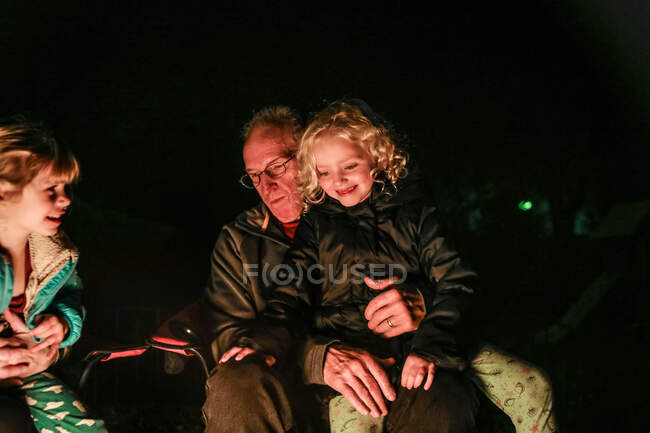 Enkelin sitzt auf Opas Schoß und sitzt an Feuerstelle — Stockfoto