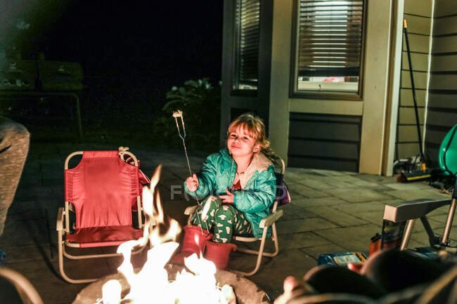 Little girl smiling while sitting in front of fire pit eating — Stock Photo