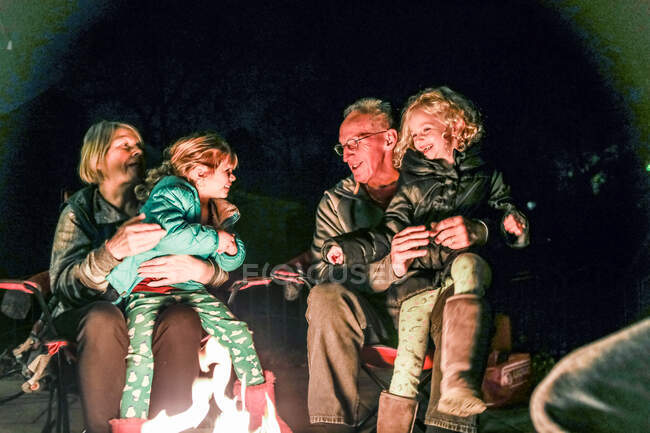 Nonni e nipoti seduti intorno al fuoco pozzo ridere — Foto stock