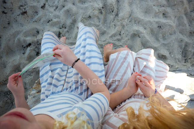 Вид сверху на девушек, сидящих на песке на пляже в платьях — стоковое фото