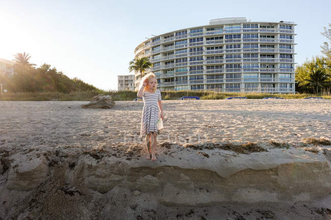 Ragazza in piedi sulla spiaggia con il sole dietro di lei guardando fuori — Foto stock