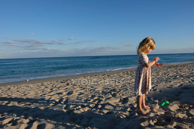 Little girl looking at her hands with back to the ocean on the beach — Stock Photo
