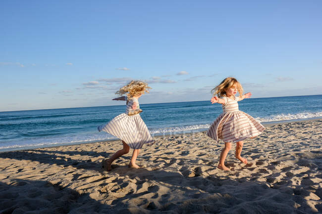 Two girls spinning on the beach with blue skies behind them — Stock Photo
