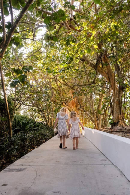 Two girls walking on path holding hands through trees — Stock Photo