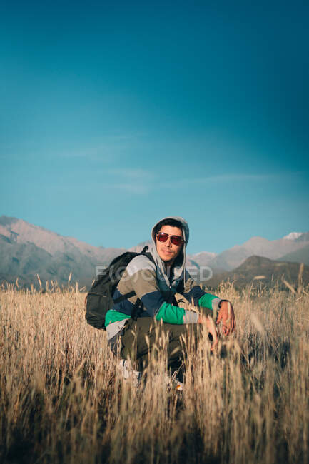 Homem com óculos de sol sorrindo no campo perto das montanhas — Fotografia de Stock