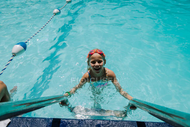 Девочка, поднимающаяся с лестницы бассейна в воде — стоковое фото