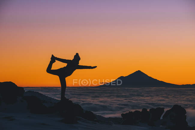 Mujer joven en postura de yoga durante el atardecer con Mt Taranaki en el fondo, Parque Nacional Tongariro, Nueva Zelanda - foto de stock