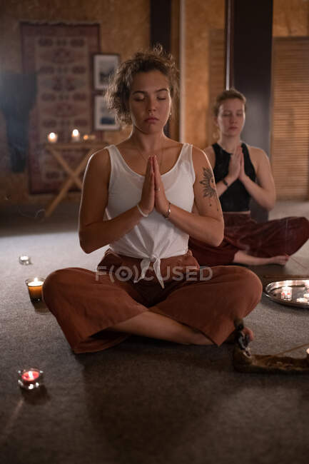 Young female friends relaxing and meditating with clasped hands in Lotus pose — Stock Photo
