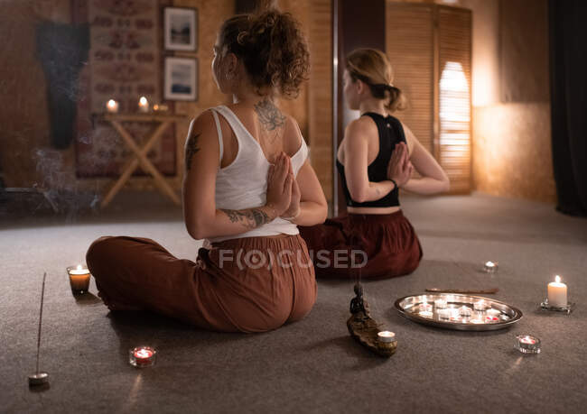 Amigos femininos anônimos apertando as mãos atrás das costas e meditando perto de velas — Fotografia de Stock